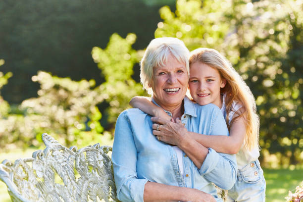 Portrait smiling grandmother and granddaughter hugging in garden  senior adult women park bench 70s stock pictures, royalty-free photos & images