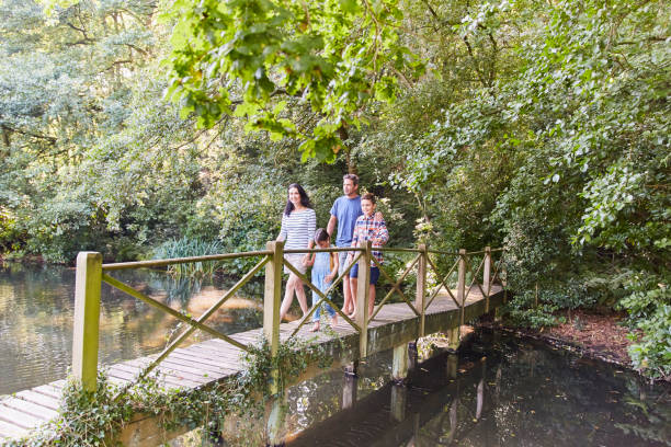 istock Family crossing footbridge in park with trees 605763627