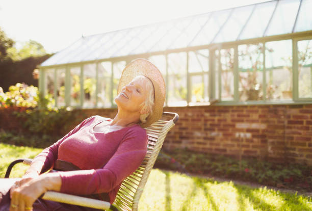 mujer mayor despreocupada relajándose fuera del soleado invernadero - tomando el sol fotografías e imágenes de stock