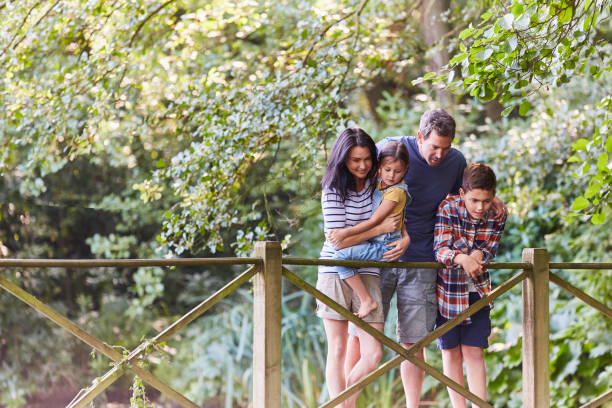 istock Family standing on footbridge in park with trees 605763859