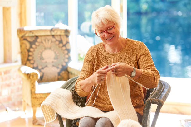 senior woman knitting in living room - tricotar imagens e fotografias de stock
