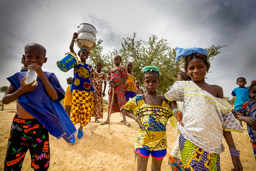 Mopti, Mali - December 31, 2016: Unidentified kids walking in the countryside, a young girl is carrying kitchenware on her head, pure African tradition. Lifestyle around Mopti in Mali 2012.