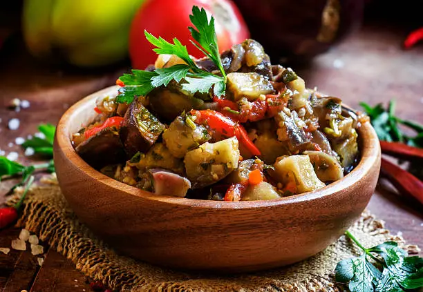 Traditional Caucasian saute from stewed eggplants, fresh vegetables and herbs on the old wooden background in rustic style, selective focus