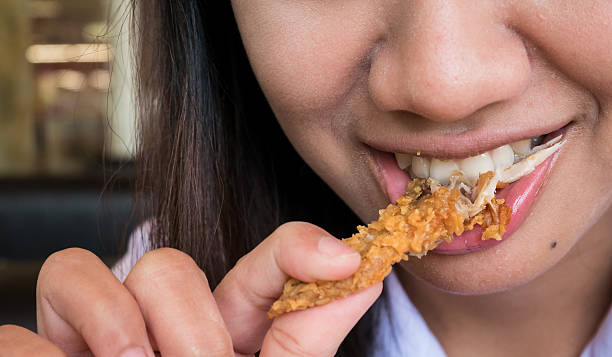 istock close up woman mouth with fried chicken 605780902