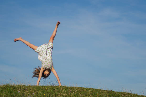 A young girl happily cartwheels on a sunny summer's day with a blue sky backdrop. 