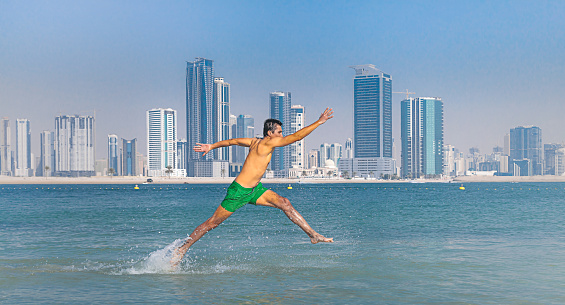 Young business man running on tropical sea or beach in motion with spray of water against city background