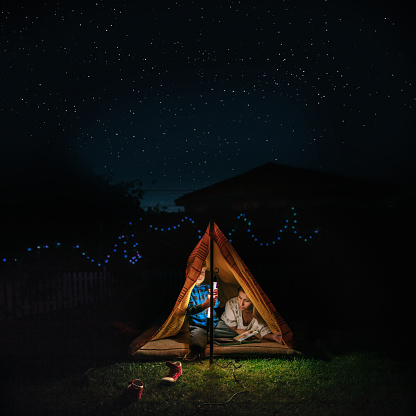 Portrait of a mother and son camping in an improvised tent in their backyard under the starry sky