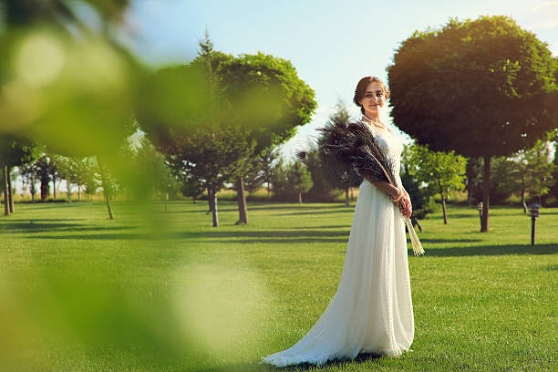 Bride holding peacock bridal bouquet in a magnificent garden.