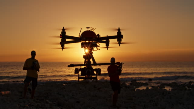 Two male operators controlling drone at sunset