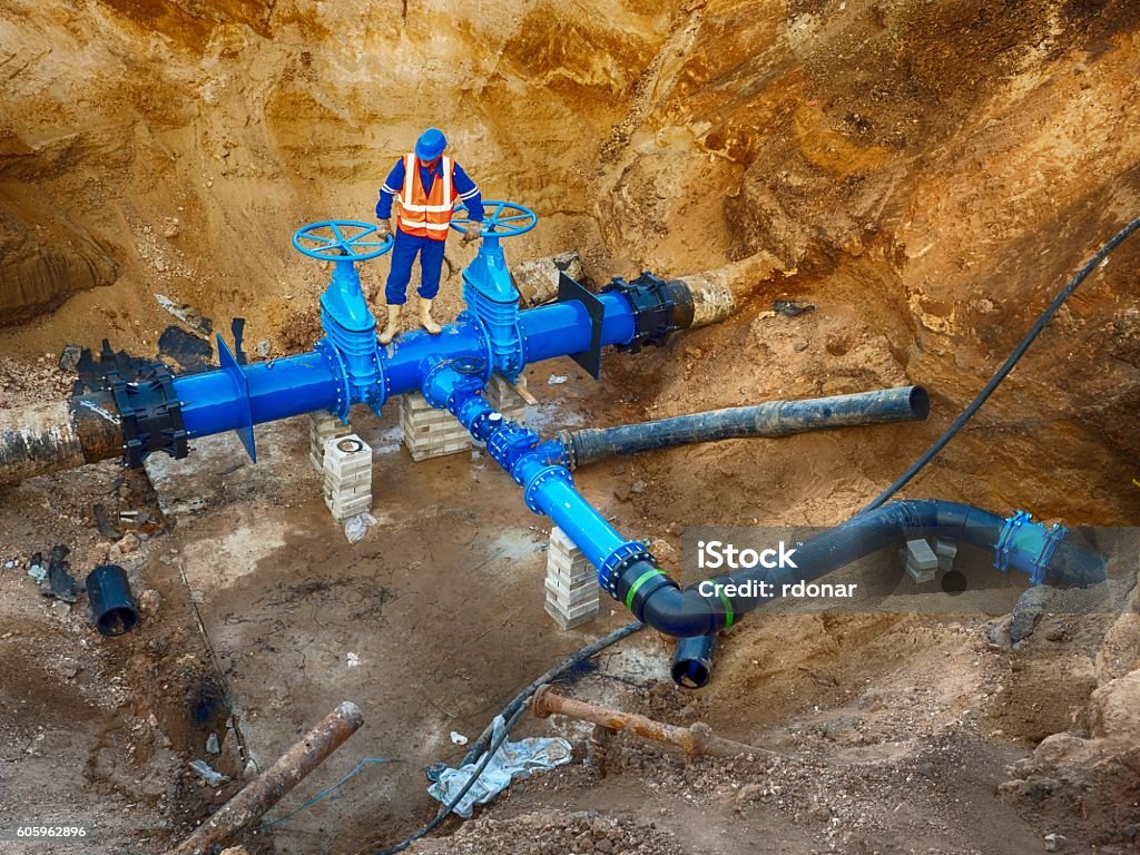 Operaio in sotterraneo sulla valvola a saracinetto, ricostruzione del sistema di acqua potabile - Foto stock royalty-free di Tubatura
