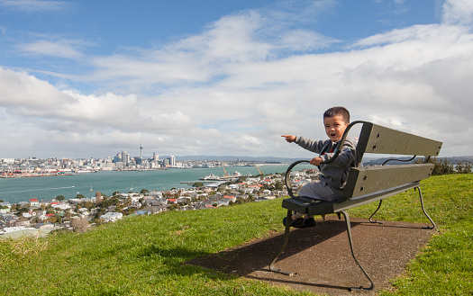 Kid sitting on a bench at Mt Victoria and pointing towards Auckland city over Devonport.