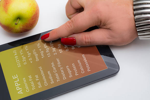 Overweight woman's hand checking the calories of an apple Overweight woman's hand checking an apple nutrients on her tablet just before eating the healthy apple joule stock pictures, royalty-free photos & images