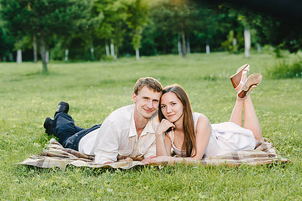 Picture of a nice couple smiling cutely to the camera Picture of a nice couple smiling cutely to the camera lying on the grass happy together. Love story in the nature cutely stock pictures, royalty-free photos & images