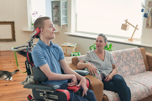 Color image of a real life young physically impaired ALS patient spending time with his mother at home. He is happy.