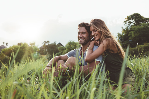 Outdoor shot of young happy lovers sitting on meadow. Happy young couple in grass.
