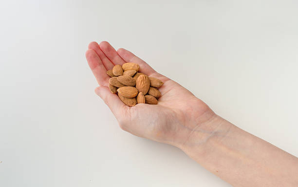 istock Woman Holding Almonds in Her Hand on a White Background 606000774