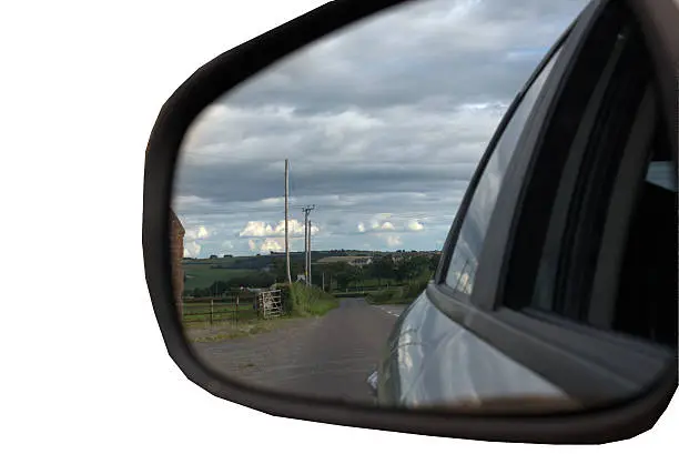 Image of a car side-mirror catching the reflection of a country road isolated against a white background