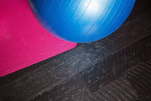 istock Blue exercise ball and pink mat on black wooden floor 606010854