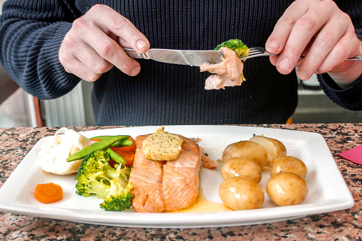 Young man eating salmon steak and vegetables in restaurant