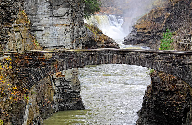 Letchworth Lower Falls Letchworth State Park, New York, is known as the Grand Canyon of the East. This is a scenic view of the stone arch bridge over Genesee River with Lower Falls in background letchworth state park stock pictures, royalty-free photos & images