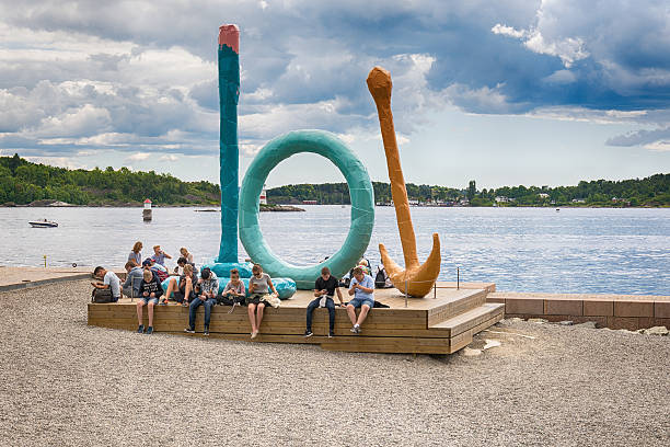 Oslo, Norway - July 18, 2016: Locals and tourists relaxing and enjoying the summer sunshine on the beach at Tjuvholmen, overlooked by the modern curves of the Astrup Fearnley Museum of Modern Art and the balconies of the waterfront apartments of Aker Brygge, the popular development overlooking Oslofjorden in the heart of central Oslo, Norway's picturesque capital city. 