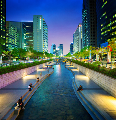Seoul Cheonggyechon River promenade at night swerving stream and high rises on each sides. Slow exposure with many people enjoying the site.