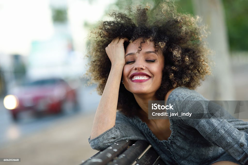 Young black woman with afro hairstyle smiling in urban backgroun Young black woman with afro hairstyle smiling in urban background. Mixed girl wearing casual clothes. African Ethnicity Stock Photo