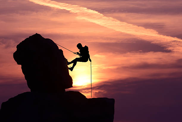 istock Man rock climber silhouette over bright sunset 606203740