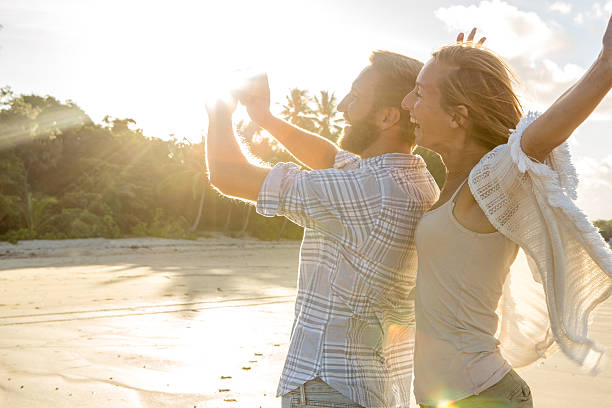 Happy couple on beach at sunset take selfie portrait Cheerful young couple on the beach take a selfie portrait at sunset. port douglas photos stock pictures, royalty-free photos & images