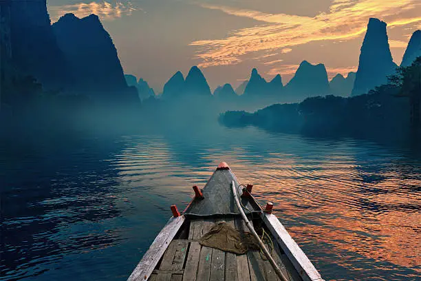 A boat riding in a river during sunset next to a beautiful mountain