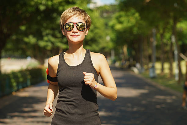 Asian woman running in sunshine in a city park stock photo