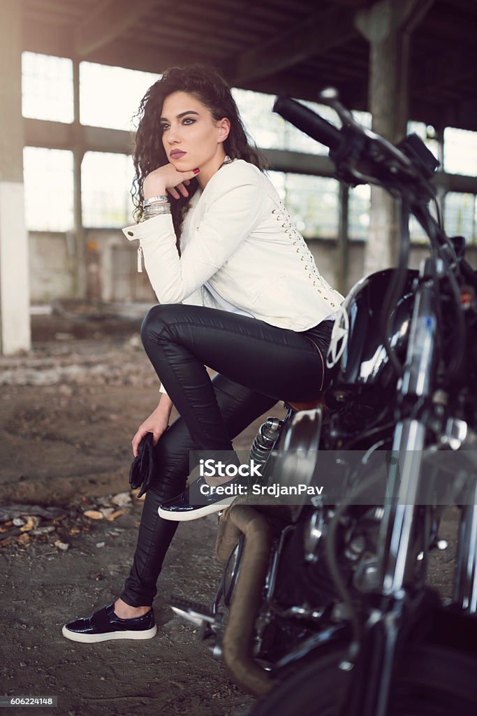 Wild Extravaganza Beautiful young woman sitting on the bike in an old ruined garage. Motorcycle Stock Photo