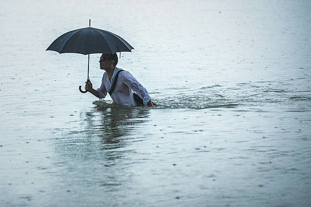 istock Handsome man holding umbrella walks through the water during rain 606230572