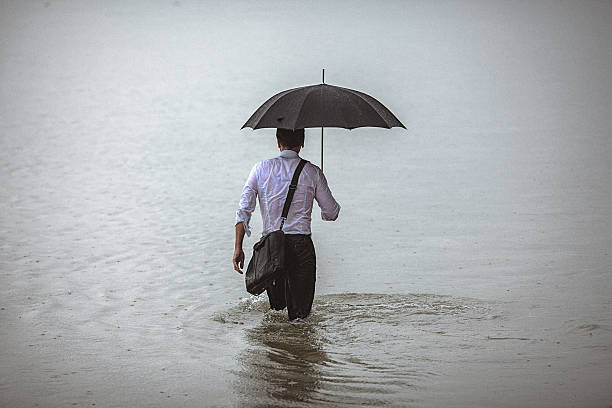 istock Handsome man holding umbrella walks through the water during rain 606230752