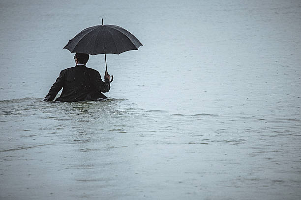 istock Handsome man holding umbrella walks through the water during rain 606230850