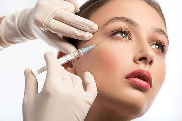 Cute girl receiving hyaluronic acid treatment Serine young woman is getting facial botox injection. Beautician hands in gloves holding syringe near her face plastic surgery photos stock pictures, royalty-free photos & images