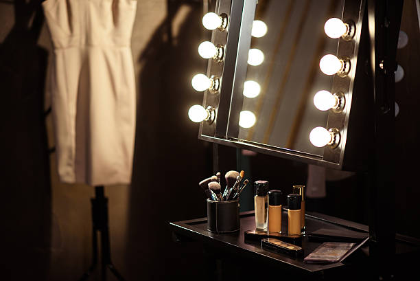 Make-up products and dress backstage Beautician cosmetics on small table near mirror with light bulbs in dressing room backstage stock pictures, royalty-free photos & images