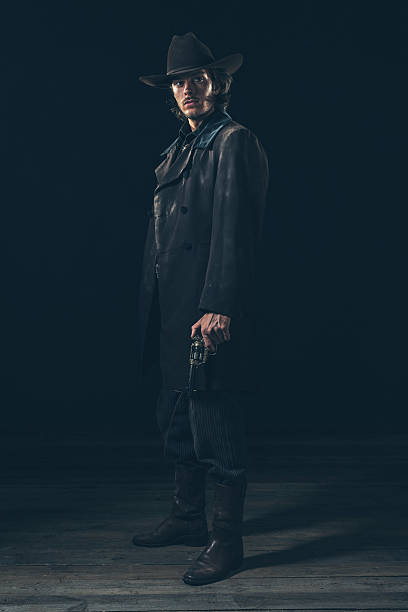 istock Menacing vintage 1900 cowboy standing with revolver. Studio shot 606642902
