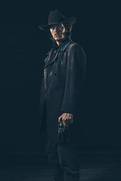 istock Menacing vintage 1900 cowboy standing with revolver. Studio shot 606642942
