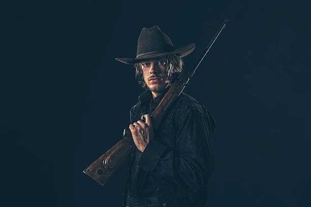 istock Retro 1900 western cowboy standing with rifle. Young man. 606652682