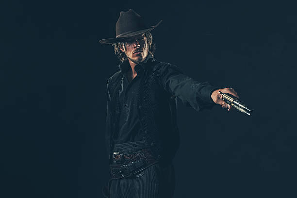 Vintage cowboy shooting with gun. Young man. Studio shot.