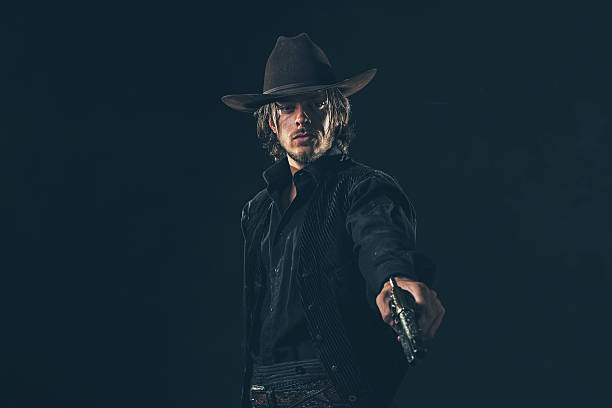 istock Vintage cowboy shooting with gun. Young man. Studio shot. 606654954