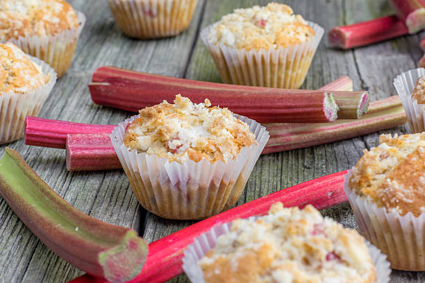 Rhubarb muffin in paper cups with rhubarb petioles Rhubarb muffin in paper cups with rhubarb petioles in the background on Old Wooden Board rhubarb photos stock pictures, royalty-free photos & images
