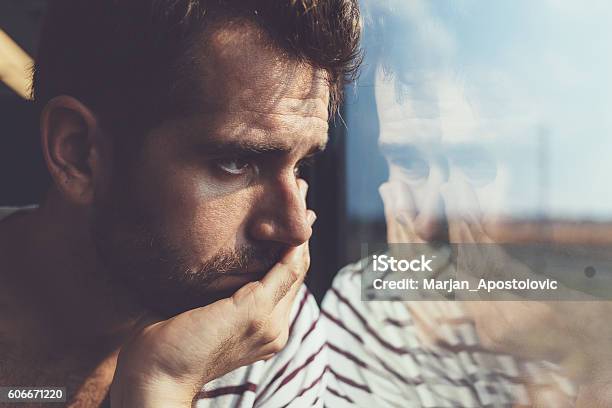 Joven Triste Mirando Por La Ventana Foto de stock y más banco de imágenes de Hombres - Hombres, Tristeza, Depresión