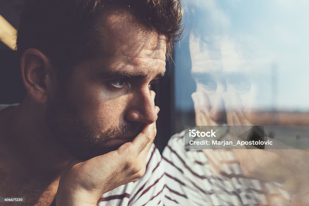 Sad young man looking through the window Men Stock Photo