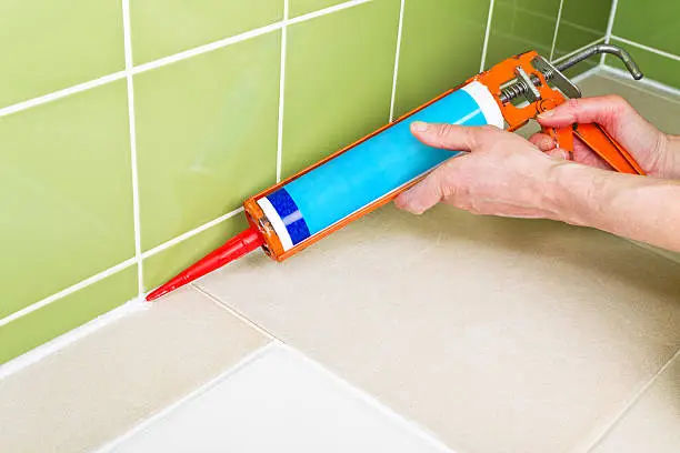 White silicone sealant being applied using a caulk gun in a bathroom shower.