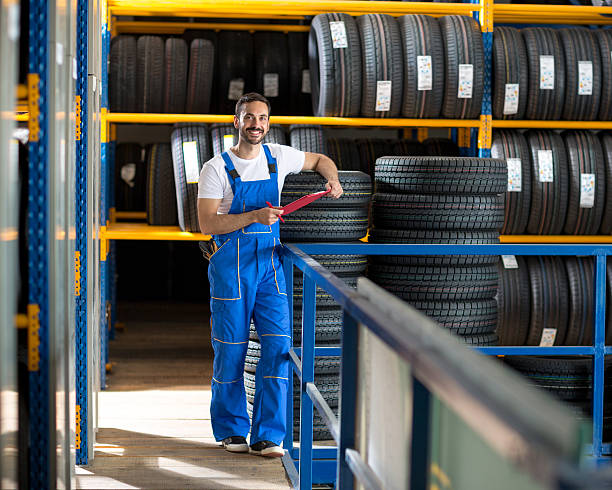 mechanik w niebieskim mundurze stojącym na oponie stockowej - tire auto repair shop part of vehicle stack zdjęcia i obrazy z banku zdjęć