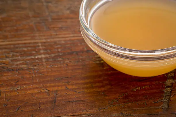 unfiltered, raw apple cider vinegar with mother  - a small glass bowl against rustic wood with a copy space