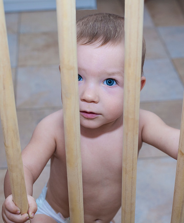 One year old baby boy behind the wooden safety gate of stairs. He is trying to go upstairs