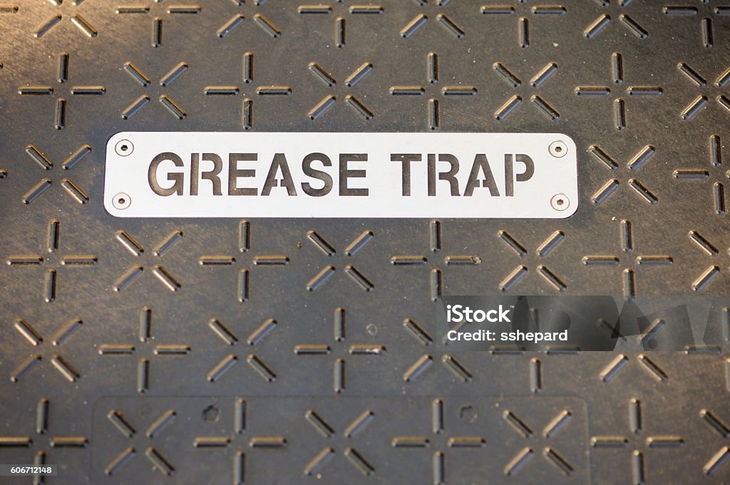 Grease trap sign on cover Close up photograph of stenciled metal great trap sign on metal cover on ground floor plate.  Plate has cross and plus sign pattern. Lubrication Stock Photo